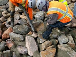 Duas pessoas utilizando mangueira para espalhar betão entre as pedras de riprap para riprap de matriz