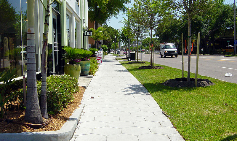 Sidewalk next to busy roadway separated by green space and trees