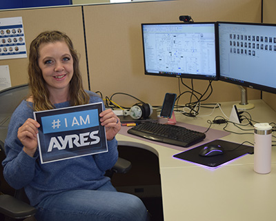 Ayres Employee-owner sitting at desk holding I Am Ayres sign.